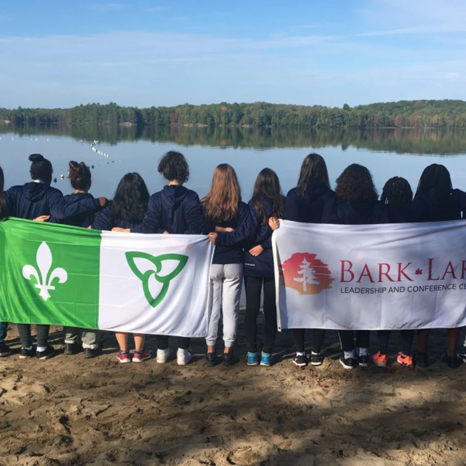 Élèves de dos, faisant face à un étendu d'eau, avec le drapeau franco-ontarien